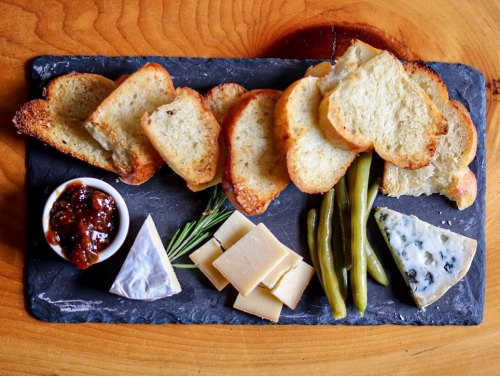 A slate platter with toasted bread, cheese varieties, green beans, and a small bowl of chutney.