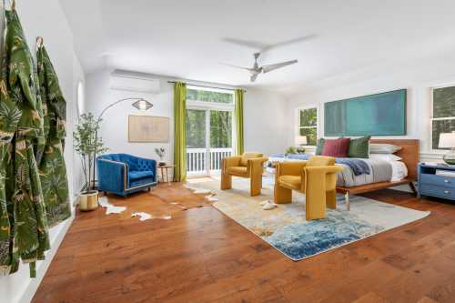 Bright, modern bedroom with a bed, yellow chairs, blue armchair, and large windows overlooking greenery.