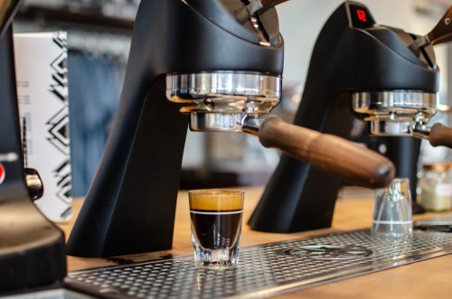 A close-up of an espresso machine with a shot of espresso in a glass on the counter.