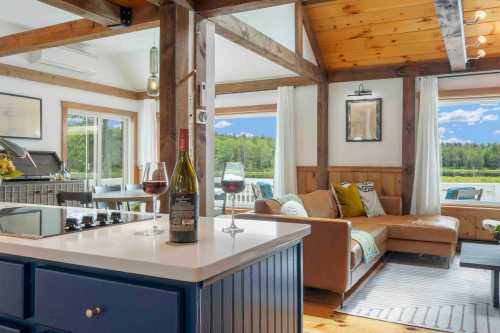 Cozy interior of a cabin with a kitchen island, wine glasses, and a living area featuring a sofa and scenic views.