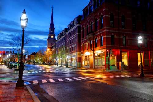 A quiet city street at dusk, featuring historic buildings, a church steeple, and glowing streetlights reflecting on wet pavement.