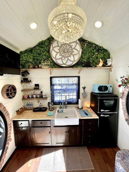 Cozy kitchen in a tiny home featuring a sink, black fridge, wooden shelves, and decorative plants. Bright and inviting space.