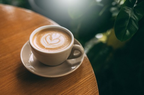 A cup of latte with a heart-shaped foam design on a wooden table, surrounded by green plants.