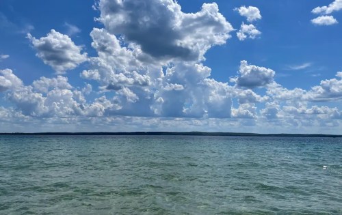 A serene view of calm waters under a bright blue sky filled with fluffy white clouds.