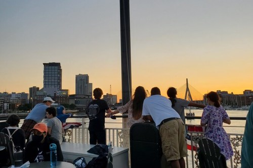 A group of people watching a sunset over a city skyline from a waterfront location.