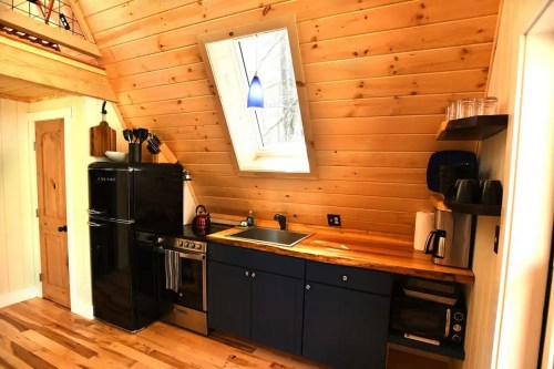 Cozy kitchen with wooden walls, black appliances, and a skylight, featuring a stove, sink, and countertop.