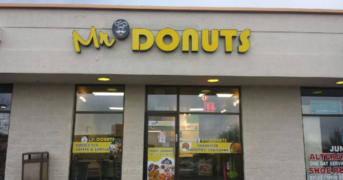 Exterior of Mr. Donuts shop with yellow signage and large windows displaying menu items.
