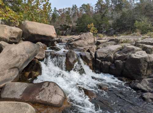 A serene waterfall cascades over rocky terrain, surrounded by trees and greenery in a natural landscape.