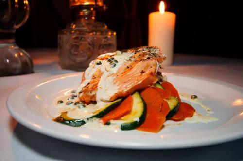A beautifully plated salmon dish with creamy sauce and colorful vegetables, illuminated by candlelight.