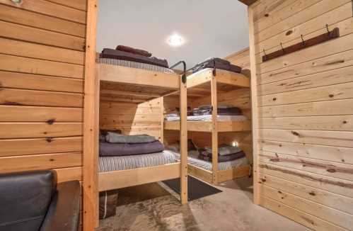 Cozy cabin interior with wooden walls and two sets of bunk beds, each with neatly arranged bedding.