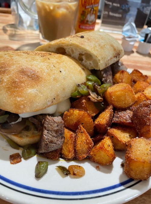 A plate featuring a sandwich with steak and peppers, alongside crispy golden potatoes.