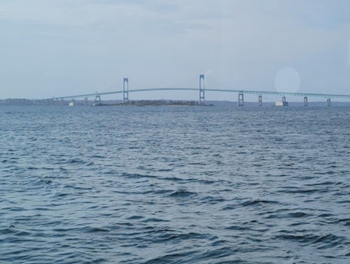 A blue bridge spans across a calm body of water under a cloudy sky.