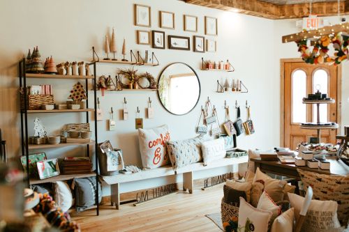 A cozy shop interior featuring shelves of decor, pillows, and a round mirror, with wooden accents and warm lighting.