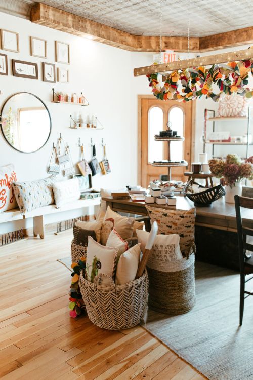 A cozy shop interior featuring decorative items, baskets of pillows, and a warm, inviting atmosphere.