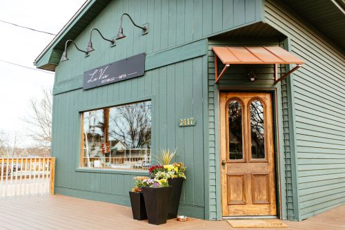 A green building with a wooden door and a sign reading "L2L" features a flower planter by the entrance.