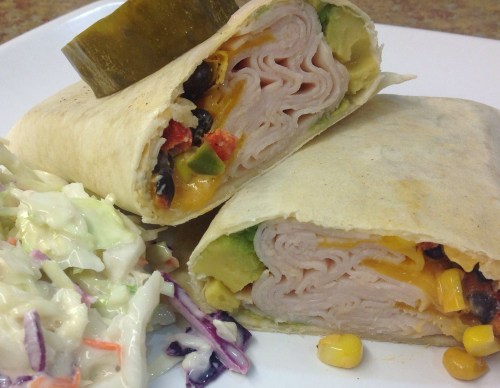A close-up of a sliced wrap filled with turkey, cheese, and vegetables, served with a side of coleslaw.