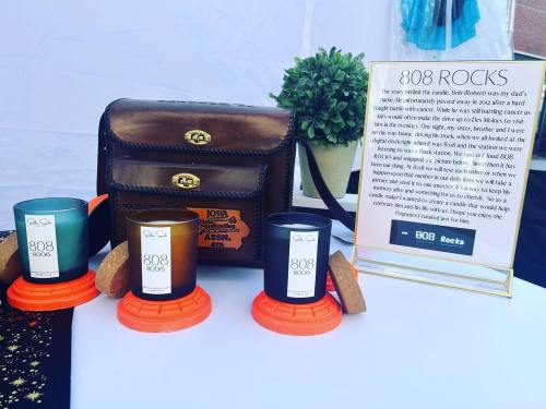A display featuring candles labeled "808 Rocks," a vintage bag, and a sign about the candles' inspiration and story.