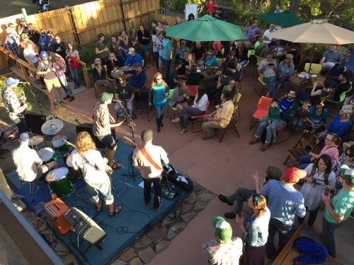 A lively outdoor concert scene with a band performing, surrounded by an engaged audience seated at tables.