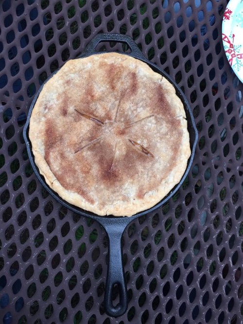 A freshly baked pie in a cast iron skillet, resting on a textured surface outdoors.