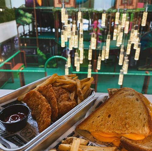 A plate with crispy chicken tenders, fries, and a grilled cheese sandwich, with a colorful play area in the background.