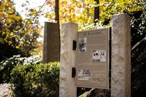 A memorial sign titled "We Remember" surrounded by trees and greenery, with historical images and text.