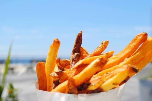 A close-up of golden, crispy French fries against a bright blue sky.