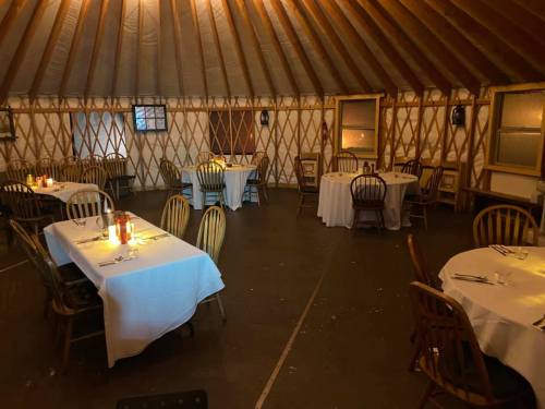 Interior of a cozy yurt dining space with tables set for dinner, soft lighting, and wooden chairs.