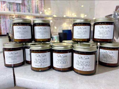 A collection of scented candles in jars, labeled with names like "Christmas Tree," "Autumn Breeze," and "Spiced Cookies."