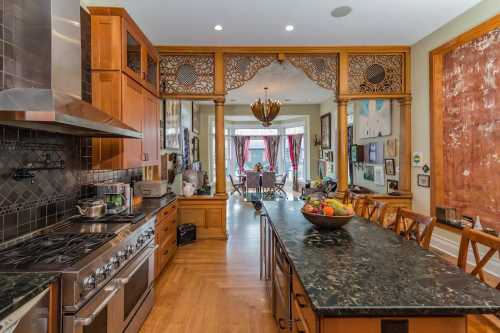 A spacious kitchen with wooden cabinets, a large island, and decorative archways leading to a bright dining area.