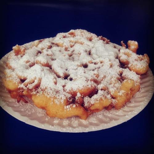 A plate of funnel cake dusted with powdered sugar, featuring a golden-brown, crispy texture.