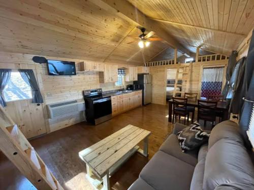Cozy wooden cabin interior featuring a kitchen, dining area, and living space with a sofa and wooden table.