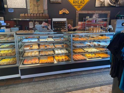 A display case filled with various baked goods, including donuts and pastries, with two people behind the counter.