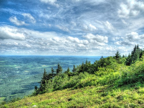 A panoramic view of lush green hills and valleys under a bright, cloudy sky.