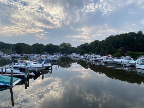 A serene marina at dusk, with boats reflected in calm water and a cloudy sky above.
