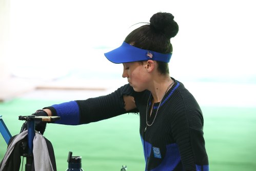 A young athlete in a blue visor and sweater adjusts equipment on a golf course, focused and determined.