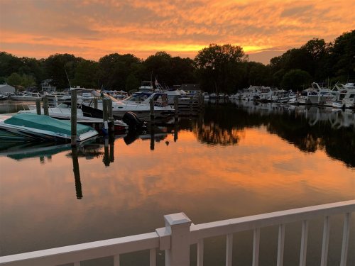 Sunset over a marina, with boats docked and vibrant orange and yellow reflections on the calm water.
