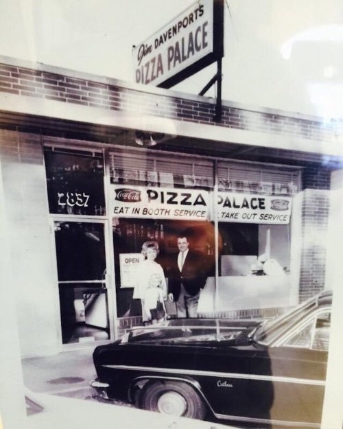 A vintage photo of Pizza Palace, featuring a couple outside the restaurant and a classic car parked nearby.