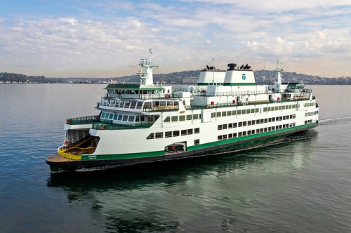 A large green and white ferry sailing on calm waters under a partly cloudy sky.
