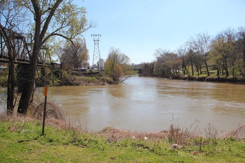 A calm river flows under a clear blue sky, with trees and power lines lining the banks.