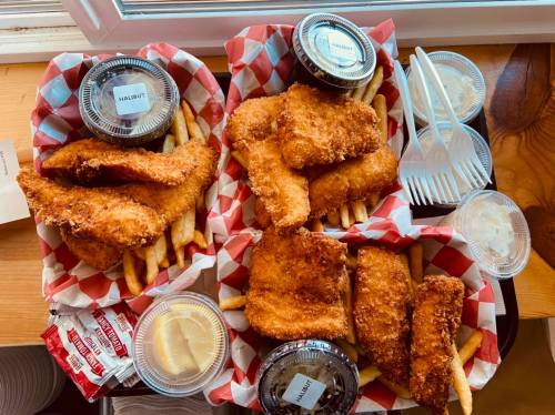 Two baskets of fried fish and fries, with dipping sauces, served on red and white checkered paper.