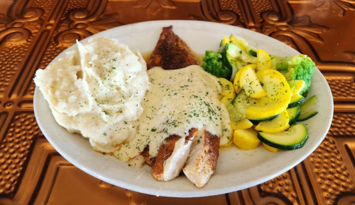 A plate featuring seasoned fish with creamy sauce, mashed potatoes, and a side of sautéed zucchini and broccoli.