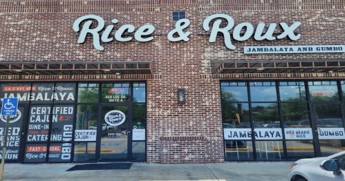 Exterior of Rice & Roux restaurant featuring a brick facade and large windows displaying the menu and "Open" sign.