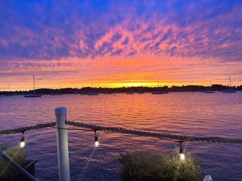 A vibrant sunset over a calm waterway, with boats anchored and colorful clouds reflecting in the sky.