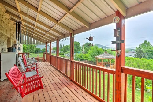 A wooden porch with red rocking chairs, overlooking a green landscape and gazebo under a cloudy sky.