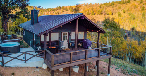 A cozy cabin with a deck, hot tub, and mountain views, surrounded by trees and autumn foliage.