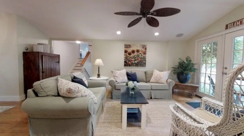 Cozy living room with a light color scheme, comfortable seating, a lamp, and a view of stairs and outdoor area.