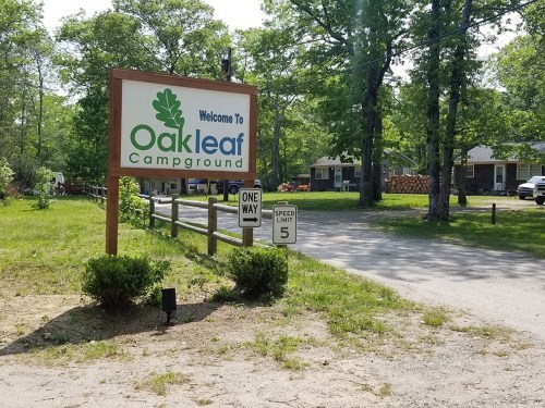 Sign for Oakleaf Campground with a one-way and speed limit sign, surrounded by trees and cabins in the background.