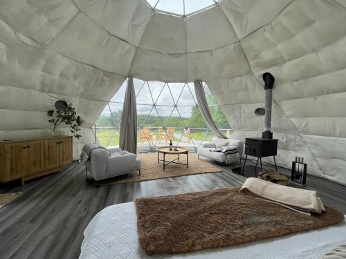 Cozy interior of a geodesic dome with a bed, seating area, and large windows overlooking nature.
