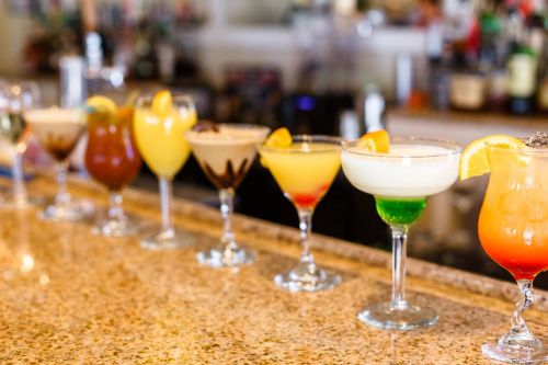 A colorful array of cocktails in elegant glasses lined up on a bar counter.
