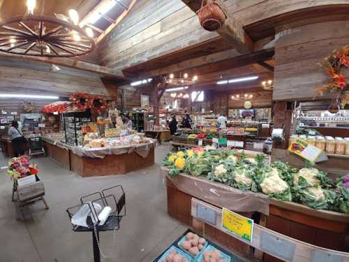 A rustic market interior filled with fresh produce, baked goods, and flowers, featuring wooden beams and warm lighting.